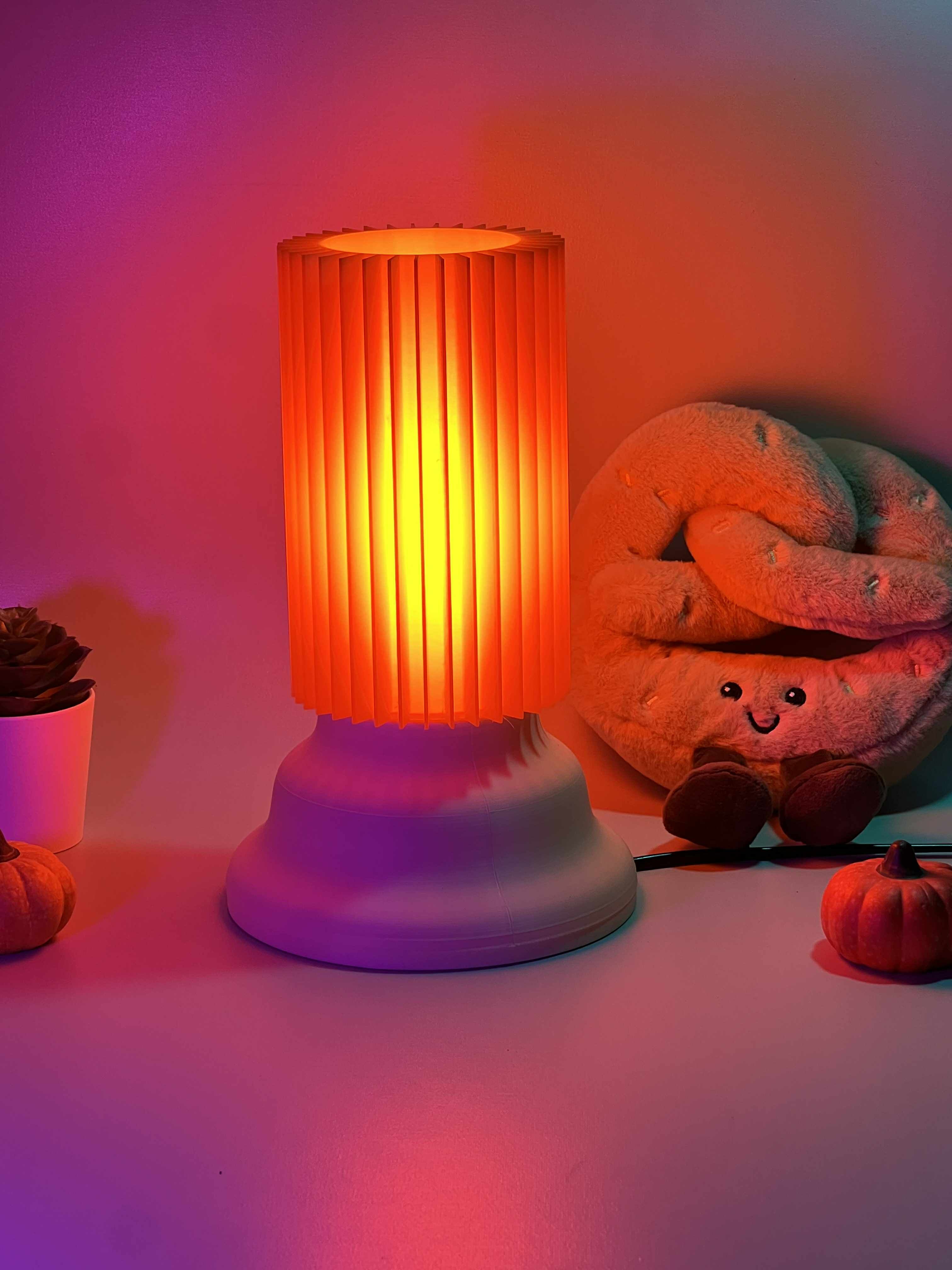 Decorative lamp with a warm glow on a surface with pumpkins and a plush toy in the background.